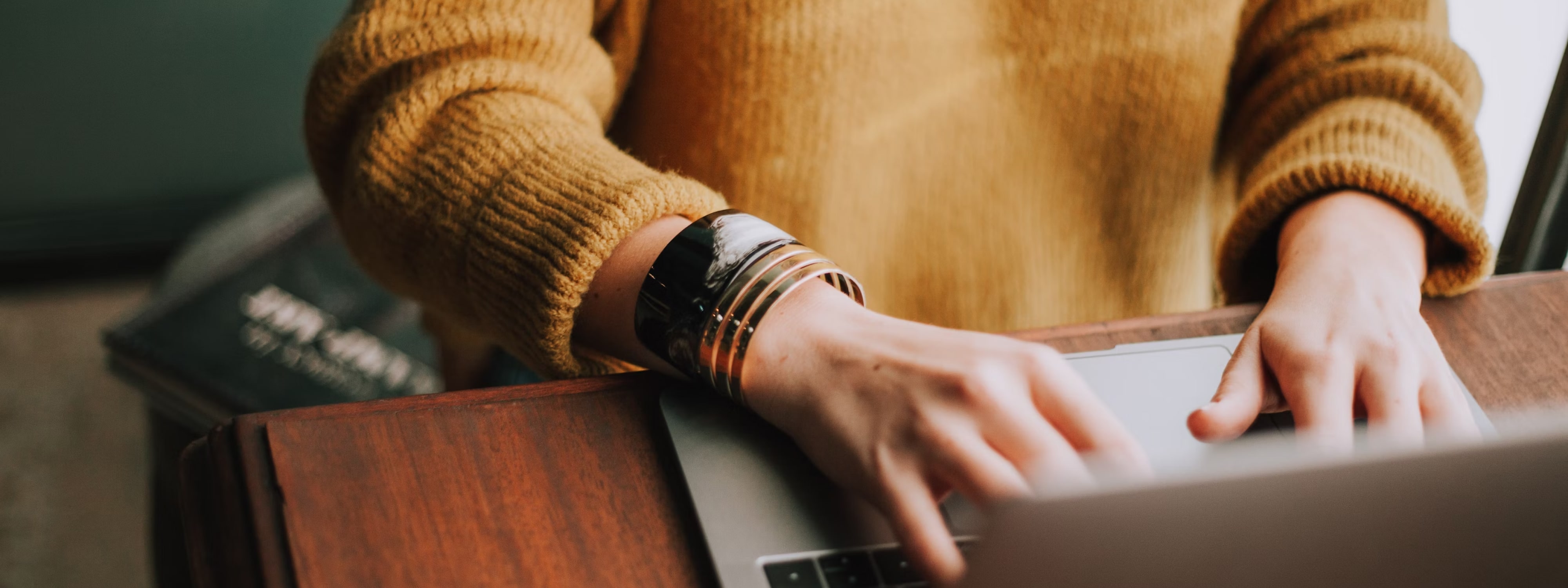 Person in mustard sweater typing on laptop with smartwatch